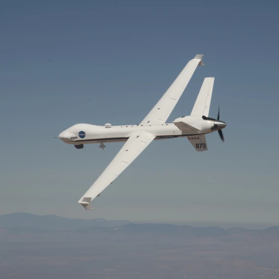 NASA's MQ-9 Predator banking in a blue sky with mountains in the background.