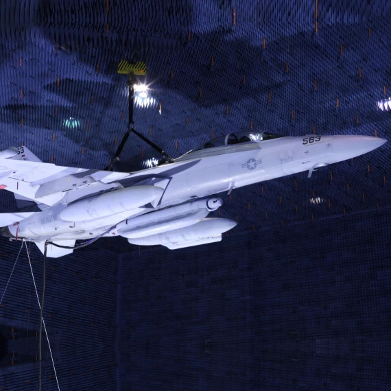 A Growler jet is shown suspended in a large anechoic chamber with three large pod-looking payloads mounted to it's belly. FIRST RF's NGJ-LB (Next Generation Jammer - Low Band) is the center pod on the belly of the aircraft.